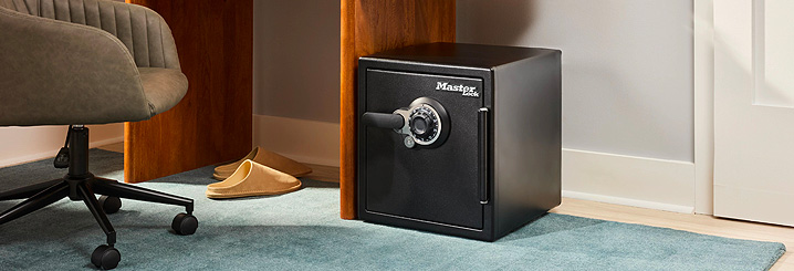 A safe sits on the floor of an office, right beside a desk. 